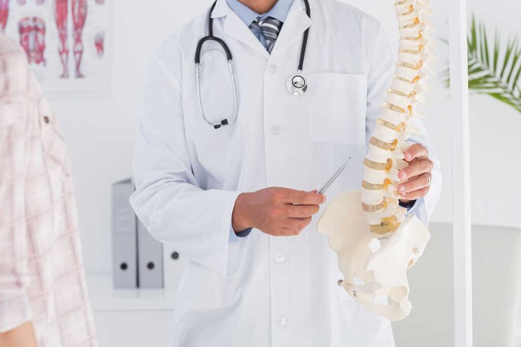 A person adjusts their ergonomic chair and computer monitor while stretching their neck at a desk.