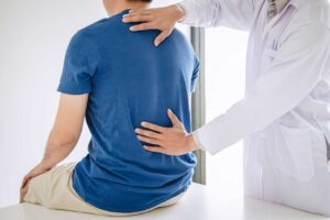 Person gently stretching beside a chair while holding a mildly sore lower back.
