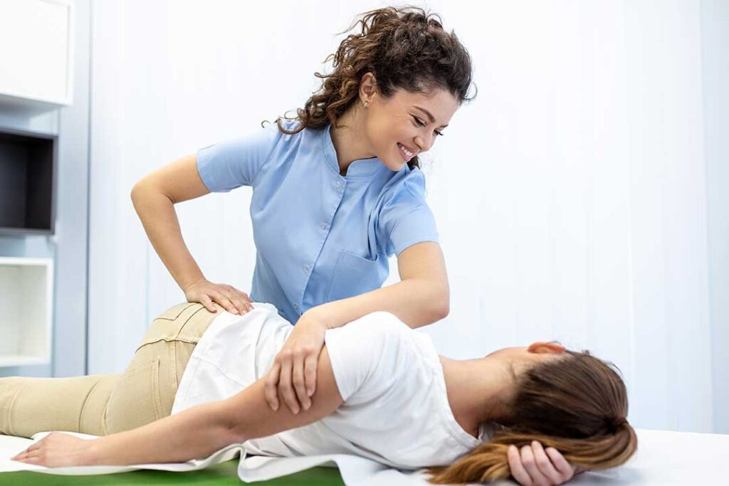 A clinician evaluates a seated adult’s shoulder and upper back movement in a bright examination room.
